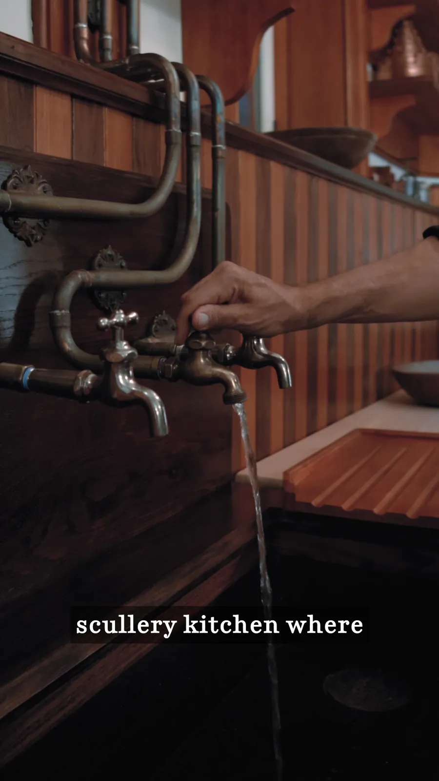 A hand turning brass taps over the copper sink in the scullery kitchen