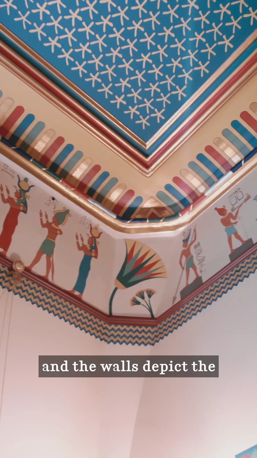 Painted ceiling of blue and white stars meeting a frieze of Egyptian-style figures